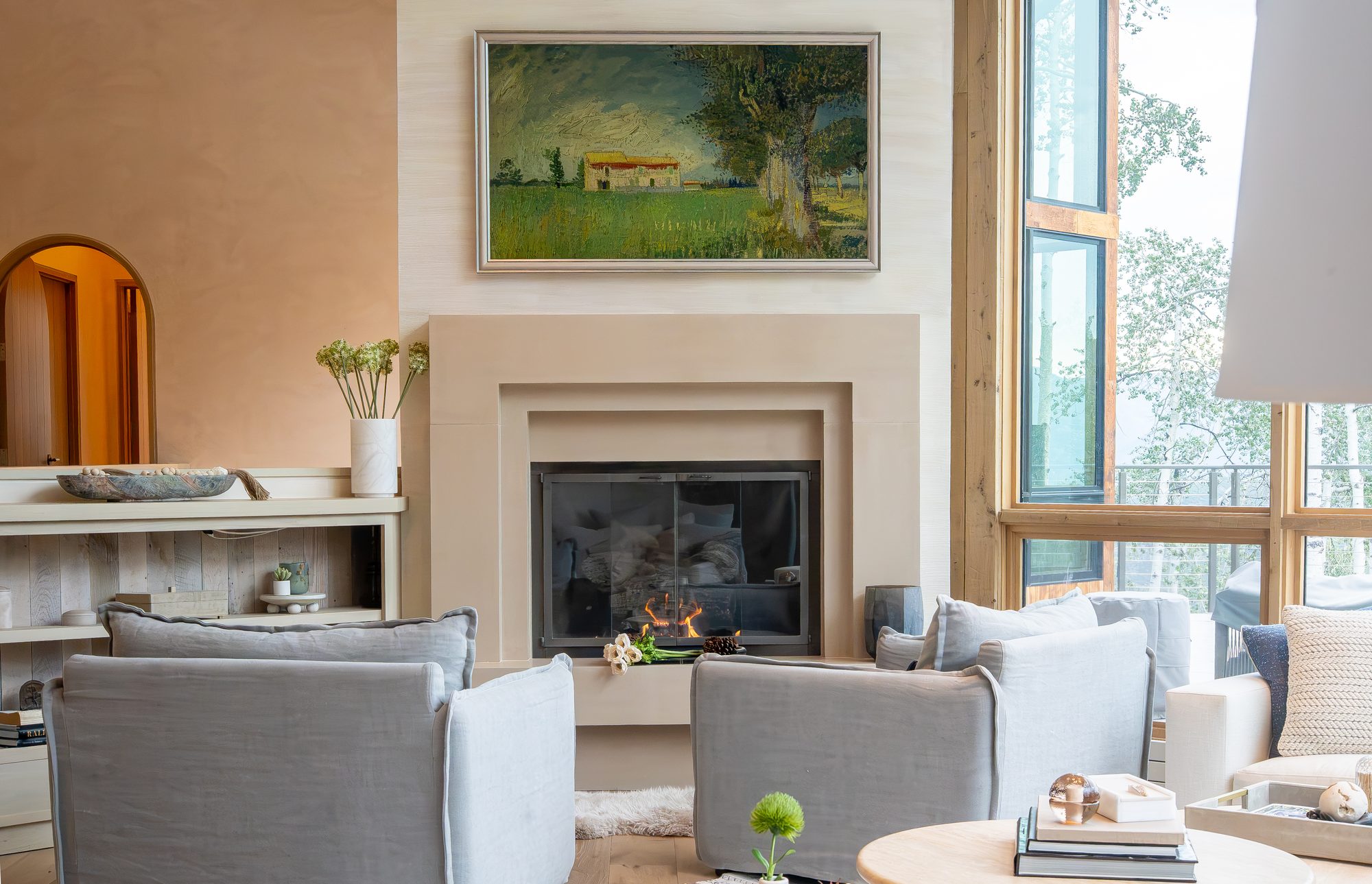 A fireplace beneath a landscape painting, afternoon